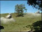 Landscape of two farming vehicles driving over a light green hill